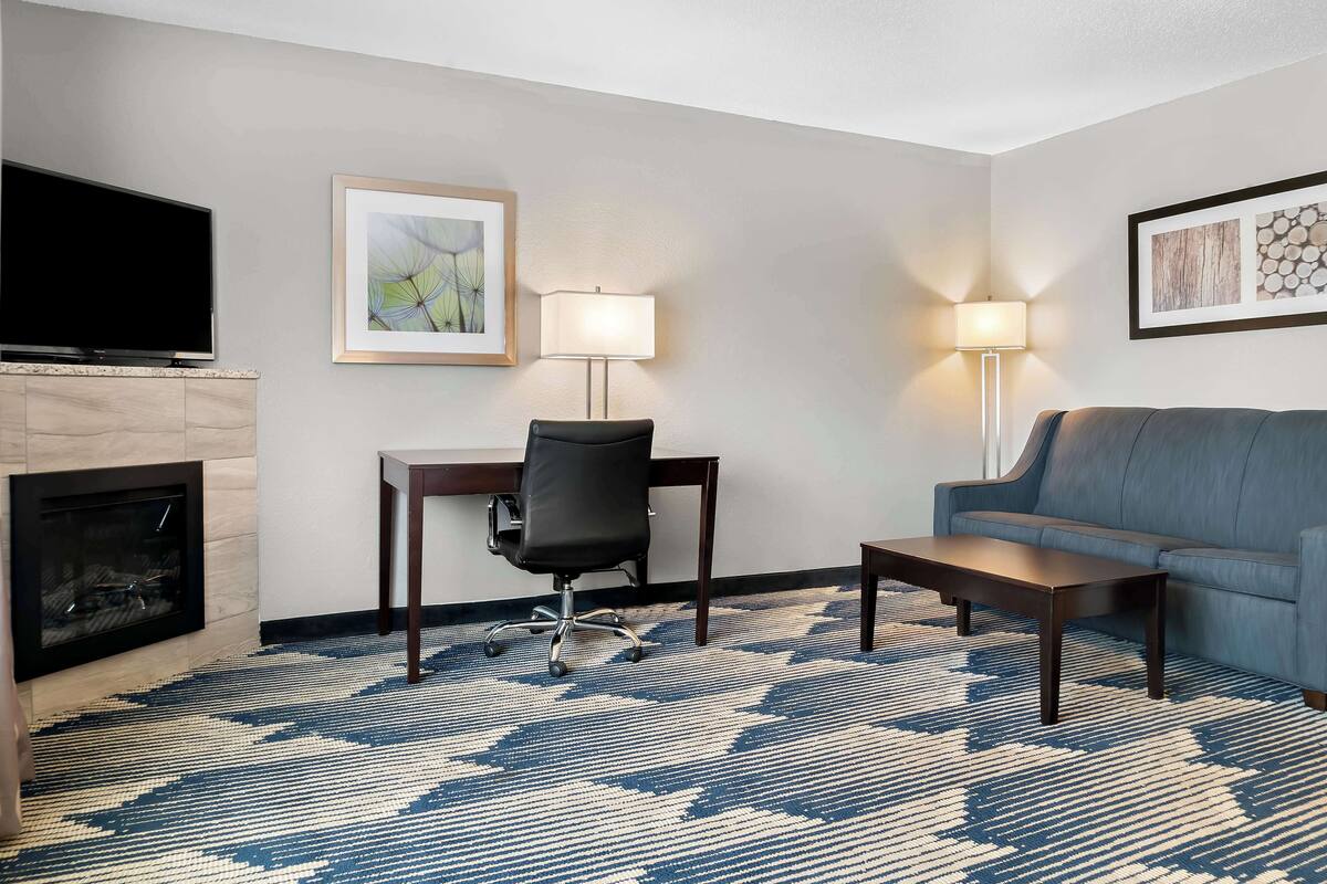 A hotel room with a flat-screen TV, a fireplace, a desk with a chair, a sofa, and two floor lamps.