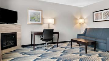 A hotel room with a flat-screen TV, a fireplace, a desk with a chair, a sofa, and two floor lamps.