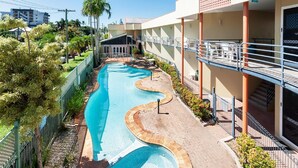 A swimming pool with a wavy design, surrounded by a brick walkway and a green fence.