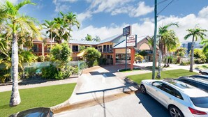 A hotel with a tropical theme, featuring palm trees and a sign indicating it is a 'Tropical Queenslander'.
