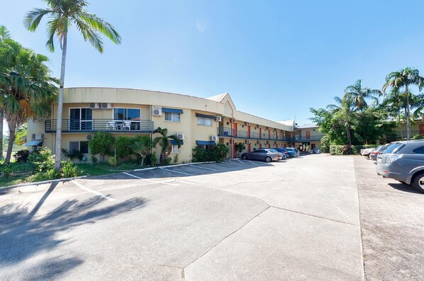 A multi-story hotel with a curved facade, outdoor seating, and a parking lot with several cars. - Tropical Queenslander (Cairns North)