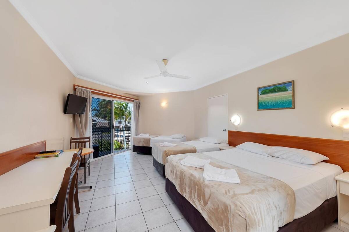 A hotel room with two beds, a desk, and a balcony with a view.