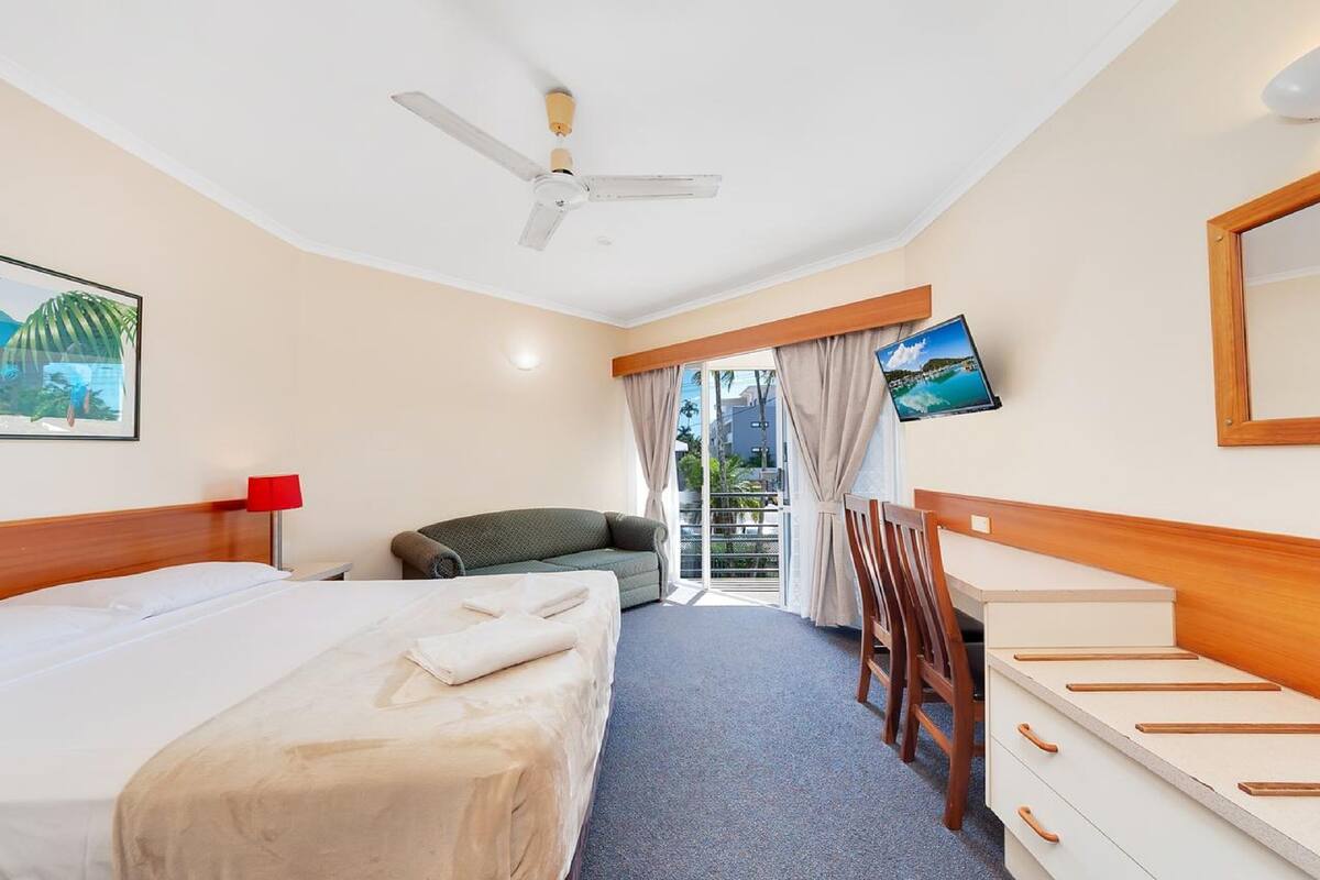 A hotel room with a bed, a desk, a chair, a television, and a window with curtains.