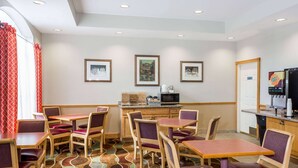 Comedor de hotel con mesas y sillas, un microondas y cuadros en las paredes.
