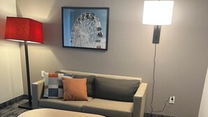 A hotel room with a sofa, a small table, a lamp, and a wall-mounted picture. - City Express by Marriott Louisville Southeast (Louisville)