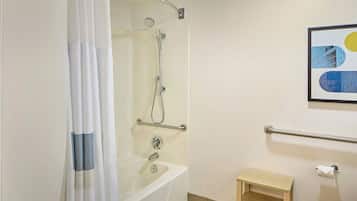 Un baño con bañera, ducha, barras de apoyo, un estante de madera pequeño y un cuadro en la pared.