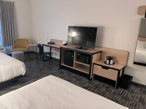 A hotel room with a bed, a desk with a TV, a microwave, and a coffee maker.