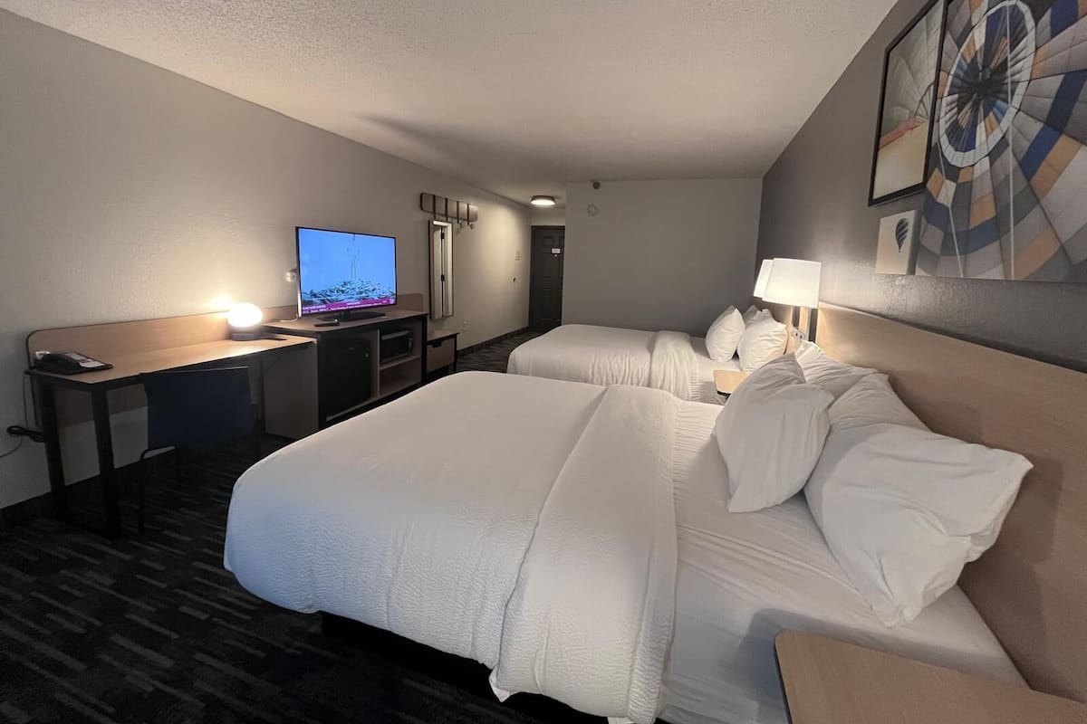 A hotel room with a large bed, a desk with a computer, a TV, and a wall-mounted artwork.