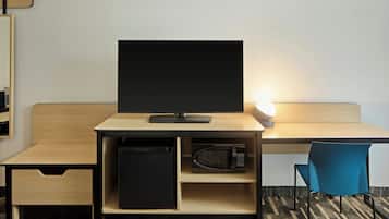 A hotel room with a desk, a television, a microwave, a trash bin, and a chair.