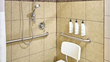 A shower area with a white chair, grab bars, and a shelf with toiletries.