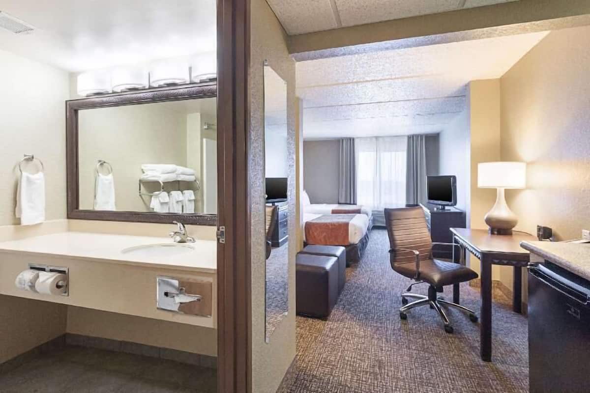 A hotel room with a bathroom, a bed, a desk, a chair, and a television.