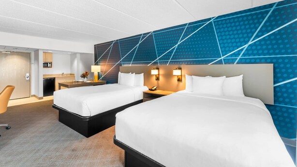Ein Hotelzimmer mit zwei Betten, einem Schreibtisch, einem Sessel und einer Küchenzeile.