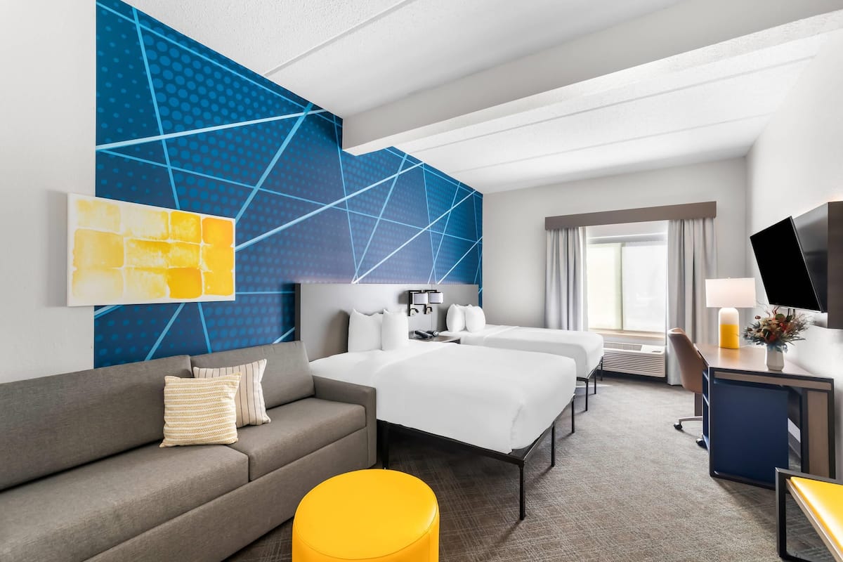A hotel room with a large bed, a sofa, a desk with a computer, and a TV.