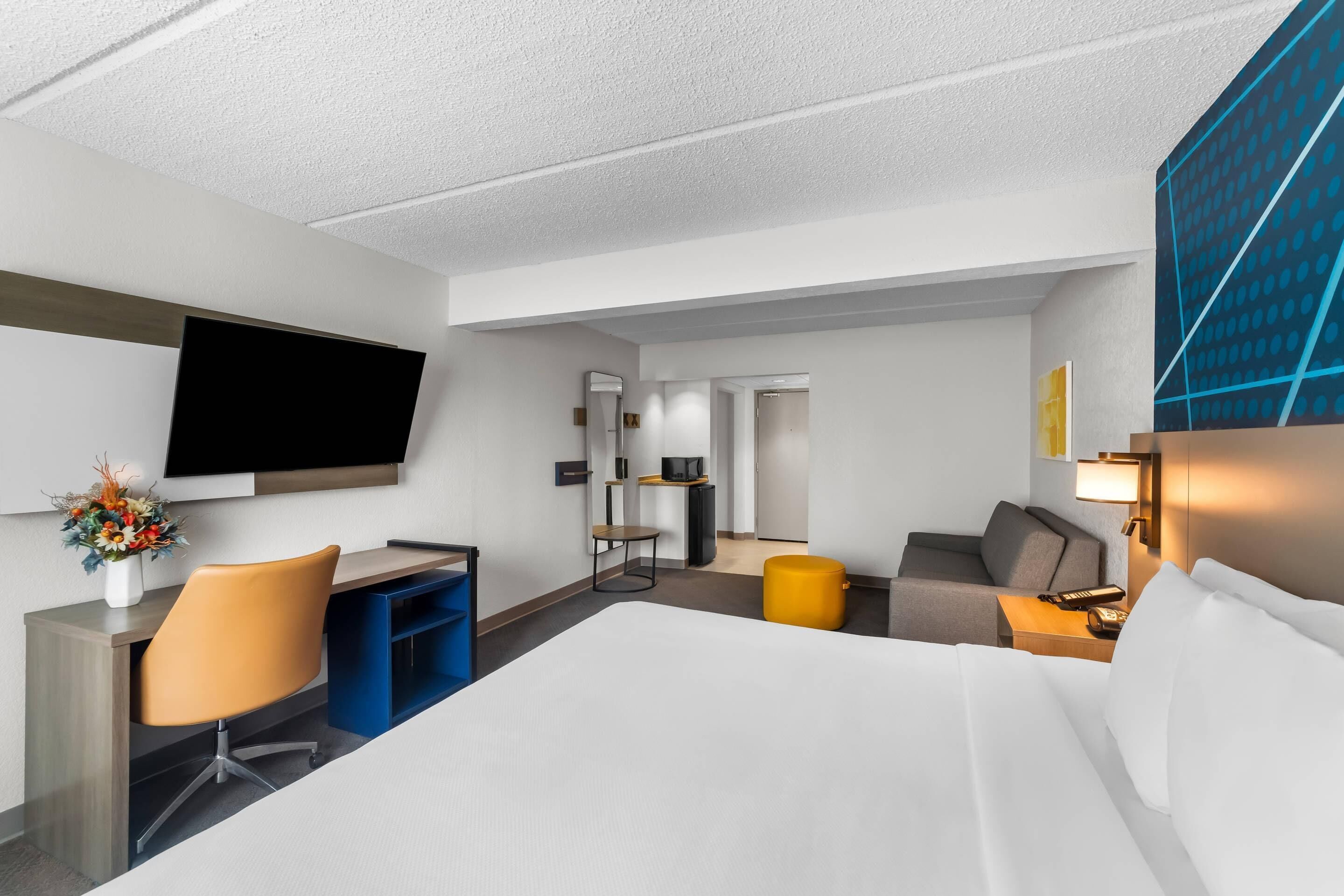 Ein Hotelzimmer mit Bett, Schreibtisch, Stuhl, Fernseher und einem kleinen Tisch mit Lampe.