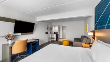 Ein Hotelzimmer mit Bett, Schreibtisch, Stuhl, Fernseher und einem kleinen Tisch mit Lampe.