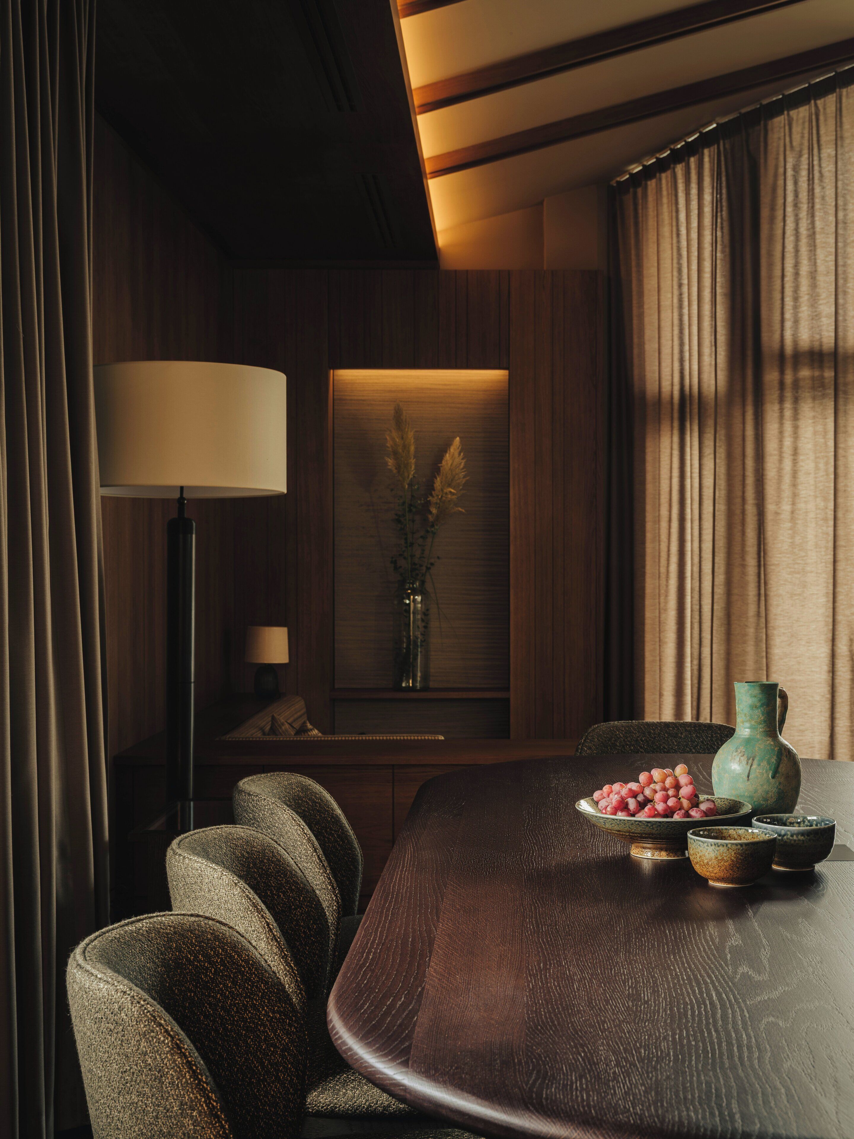 A dining area with a wooden table, chairs, a vase with flowers, and a lamp.
