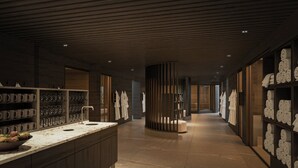 Un moderno vestíbulo de hotel con un mostrador de recepción de mármol, una columna central y estantes con toallas.