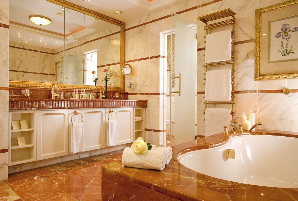 Ein luxuriöses Badezimmer mit großem Spiegel, Marmorboden, einer Badewanne und einem Waschtisch mit goldener Rahmung.