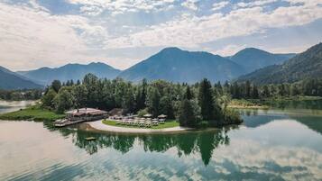 Ein Seehotel mit Steg, Außenbestuhlung und Blick auf die Berge.