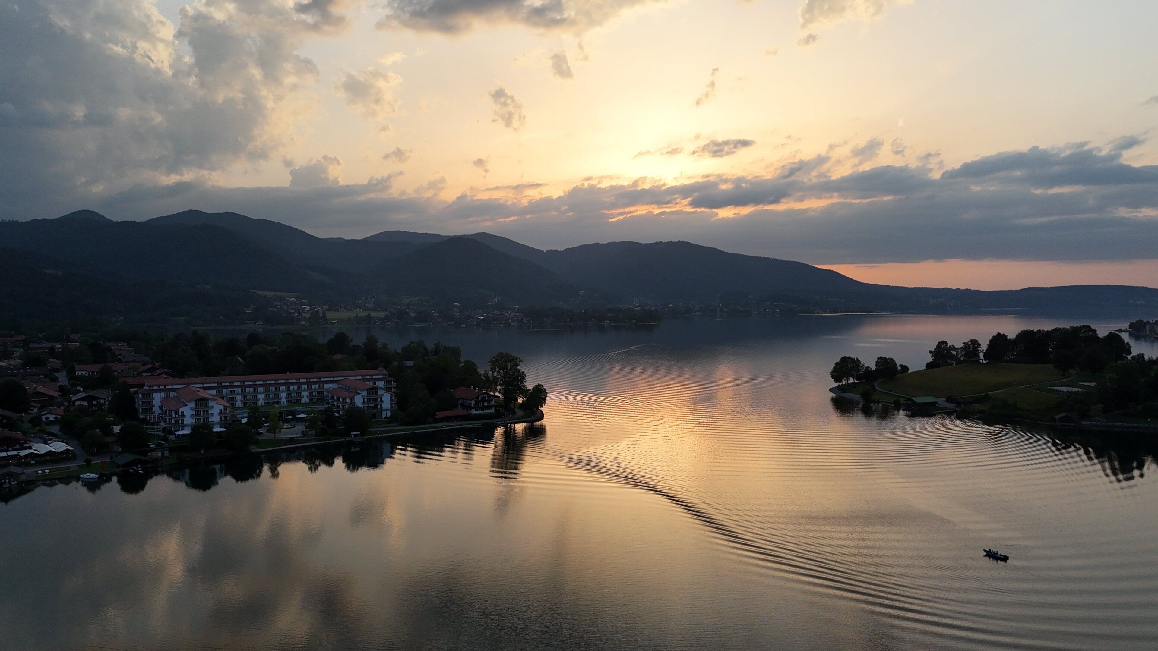 Ein ruhiger See mit Spiegelung von Gebäuden und Bergen im Hintergrund.