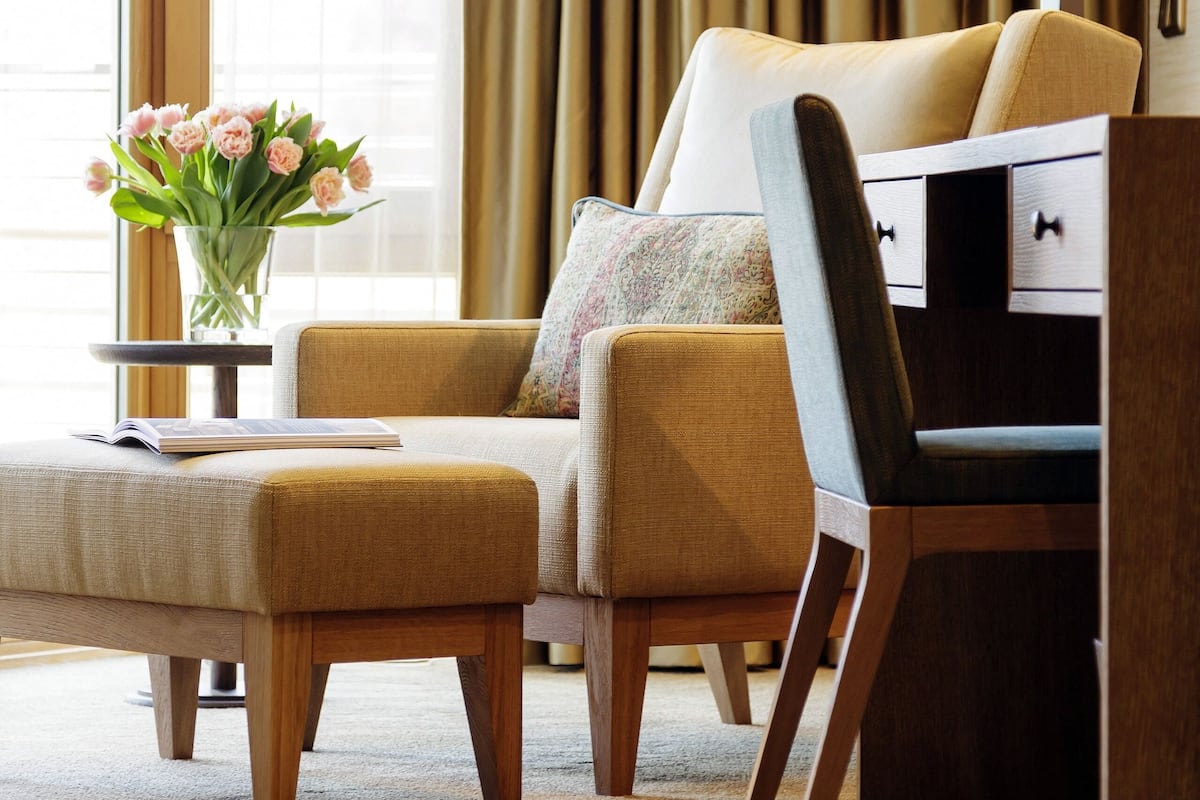 Ein Hotelzimmer mit einer Couch, einem Beistelltisch mit Blumenvase, einer Lampe und einem Holztisch.