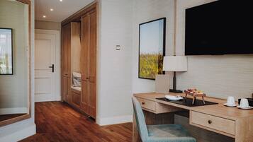 A hotel room with a wooden desk, a chair, a TV mounted on the wall, and a wardrobe.