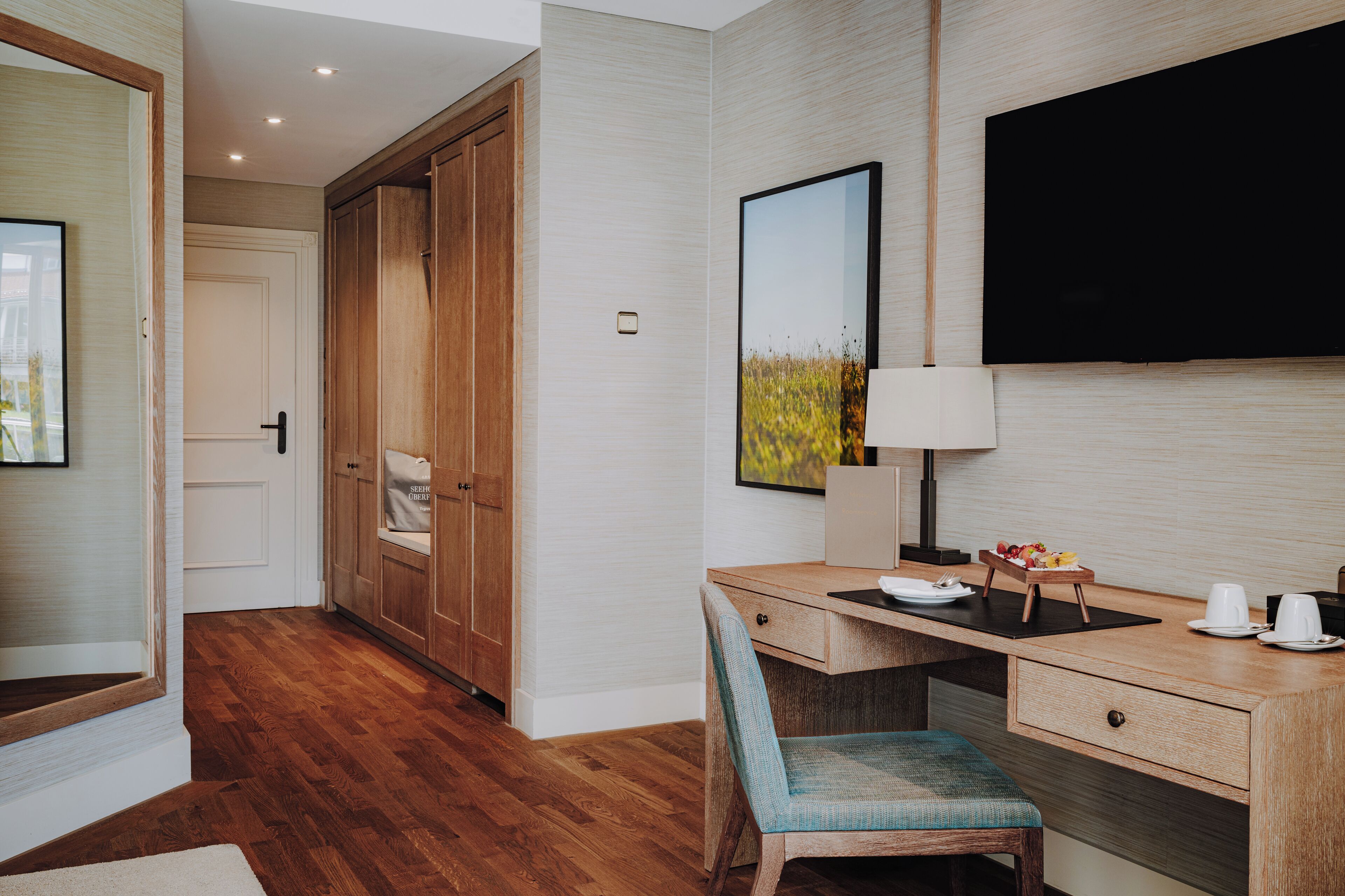 A hotel room with a wooden desk, a chair, a television, and a wardrobe.