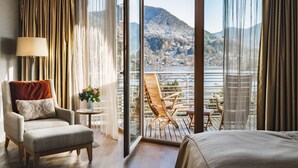 Habitación de hotel con un amplio ventanal corredero que da a un balcón con vista a un lago y montañas.