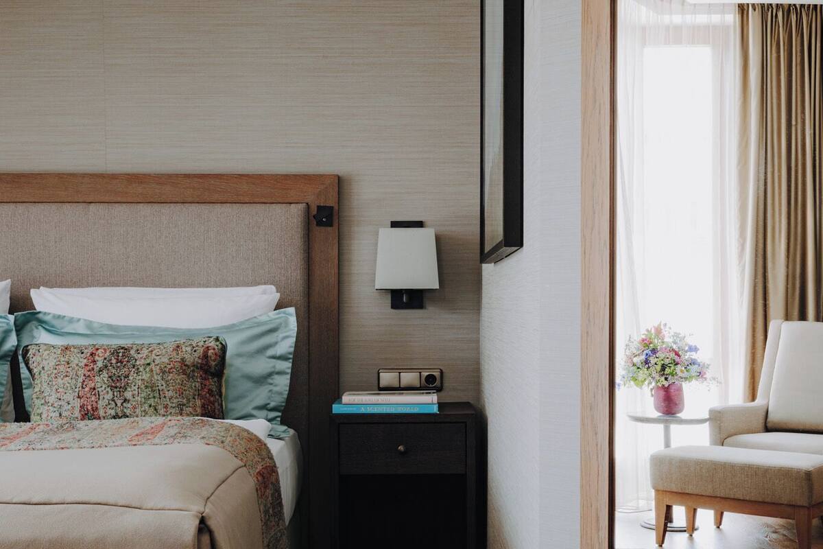 Ein Hotelzimmer mit Bett, Nachttisch, Lampe, Sessel und Blick ins Freie.