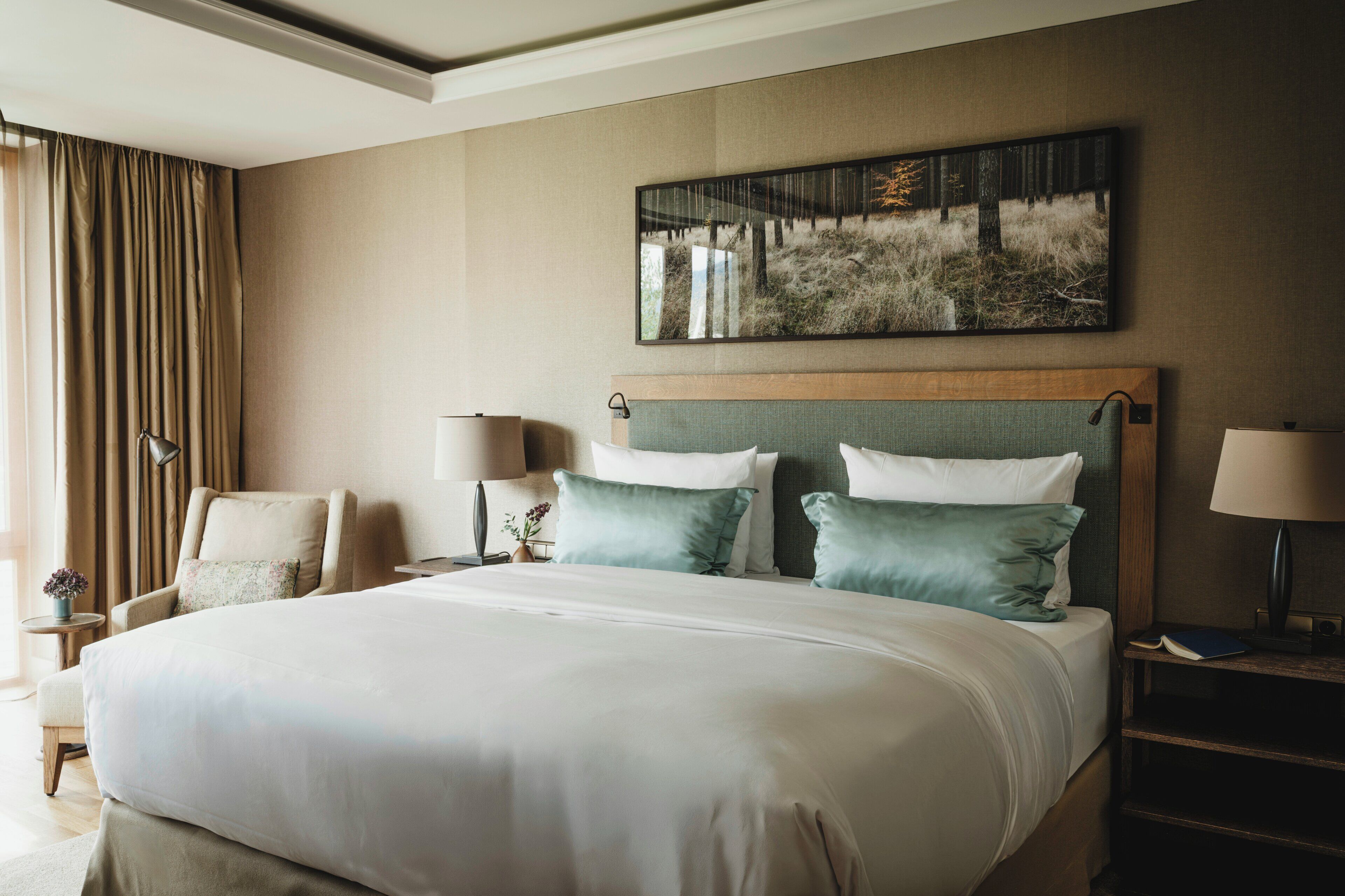 A hotel room with a large bed, two bedside tables with lamps, a chair, and a painting on the wall.