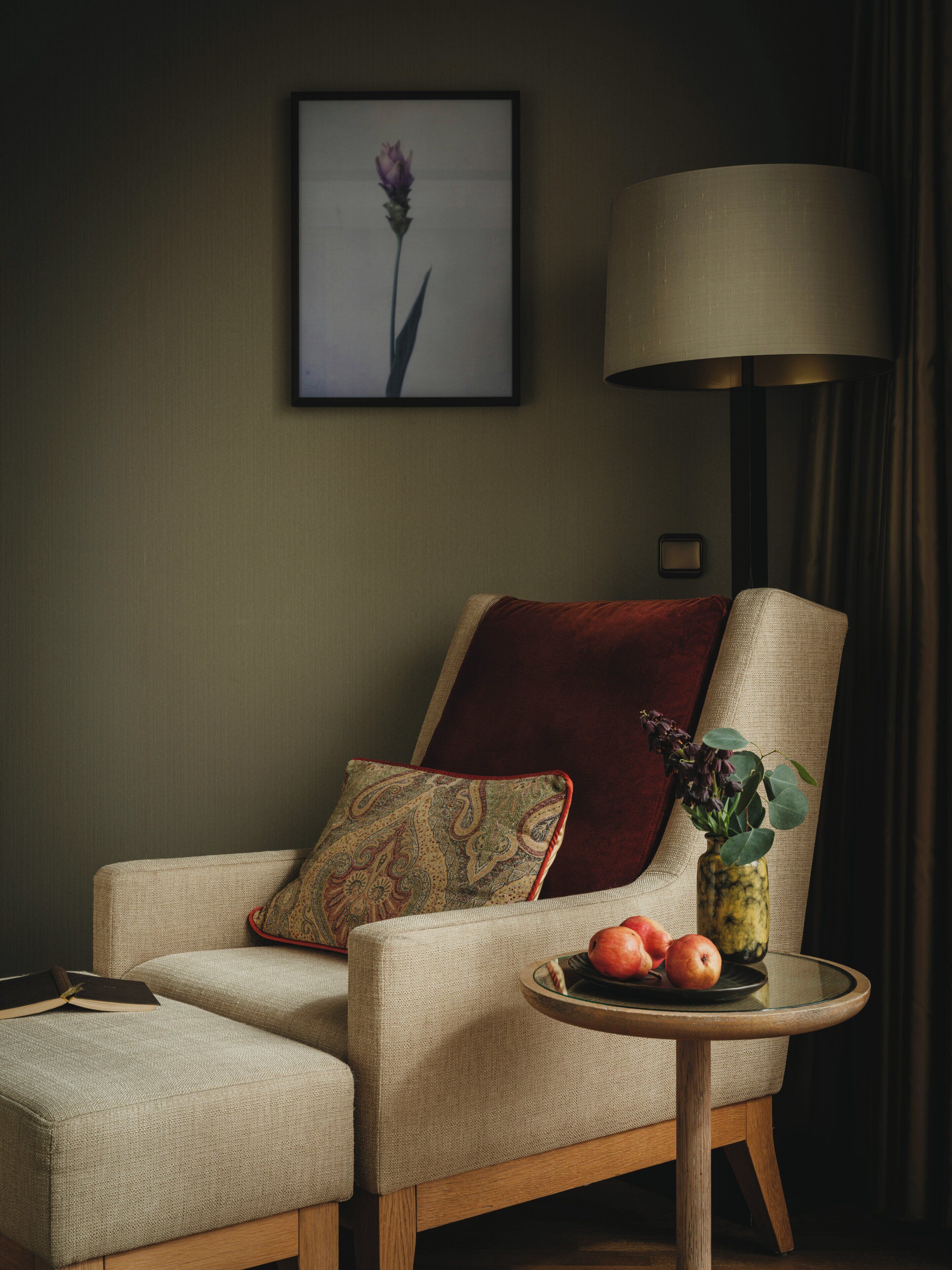 Een kamer met een bank, een klein tafeltje met fruit, een lamp en een lijst met een afbeelding aan de muur.