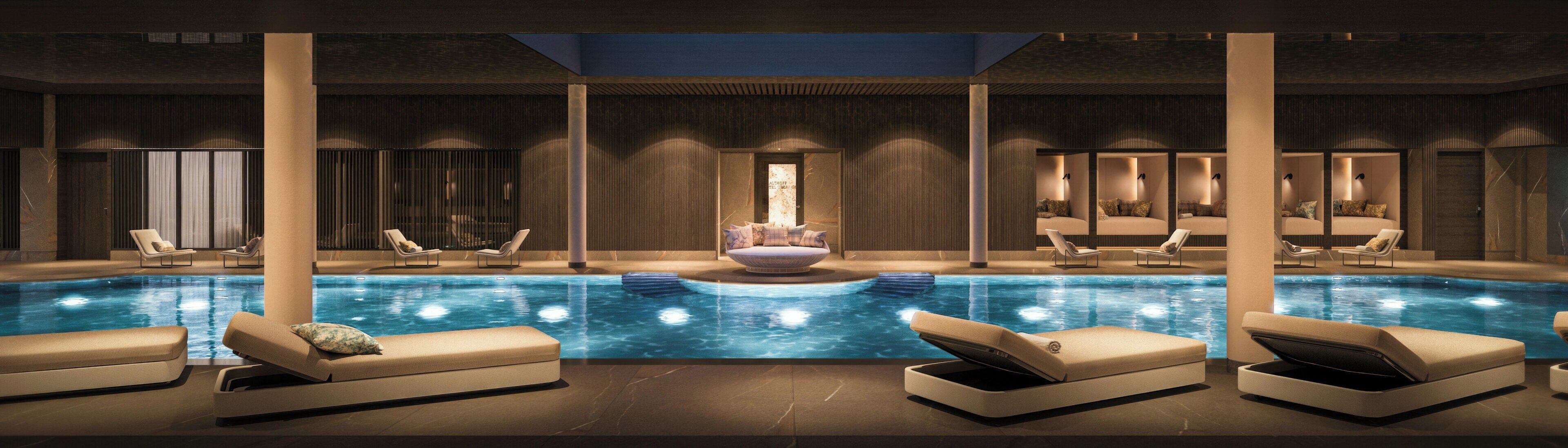 A modern indoor pool with lounge chairs and a central seating area.