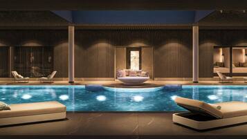 A modern indoor pool with lounge chairs and a central seating area.