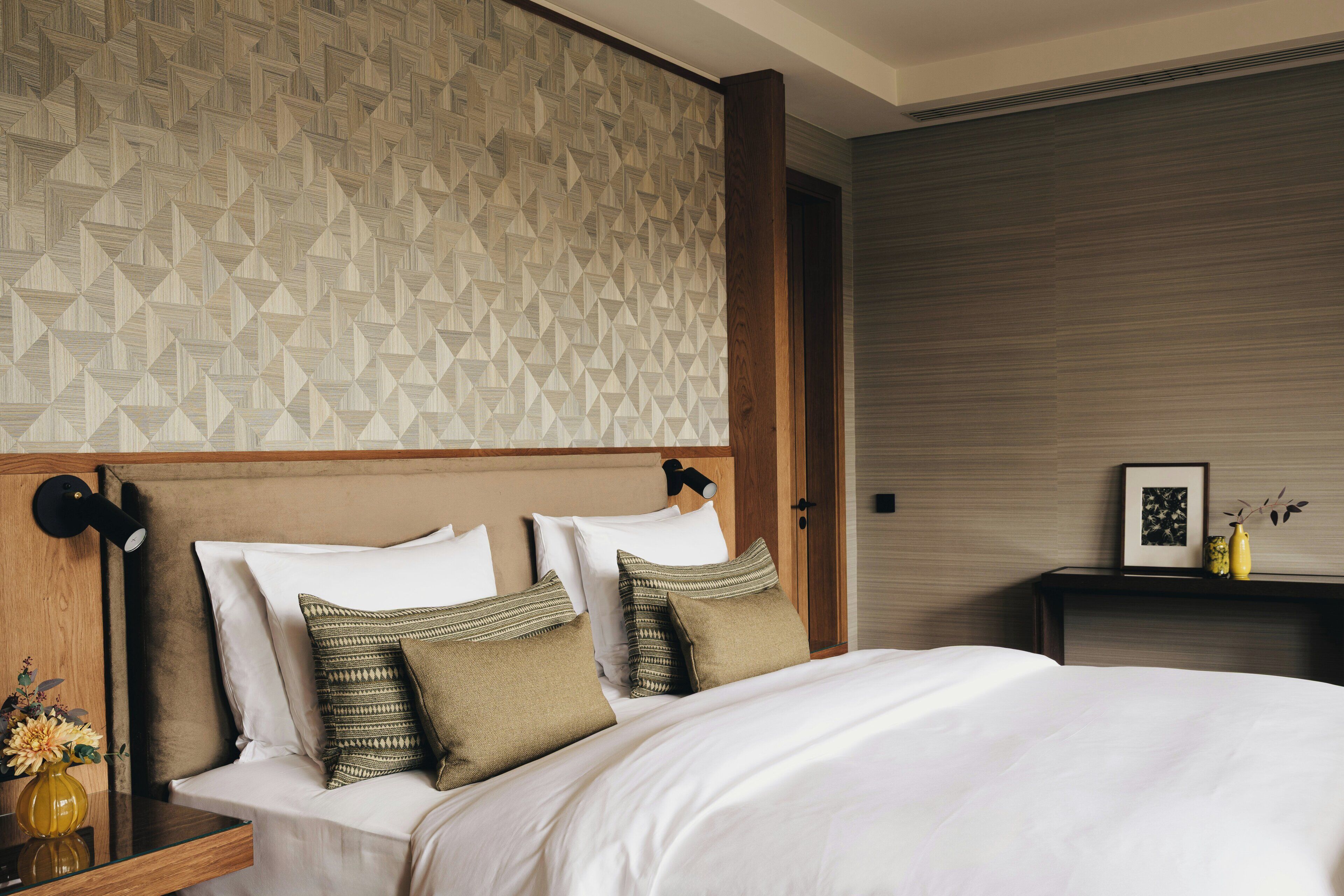 A neatly made bed with pillows, a bedside table with a vase, and a wall with a geometric pattern.