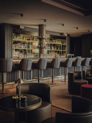 A bar area with multiple seating options, a central column, and shelves stocked with bottles. - Althoff Seehotel Überfahrt (Rottach-Egern)