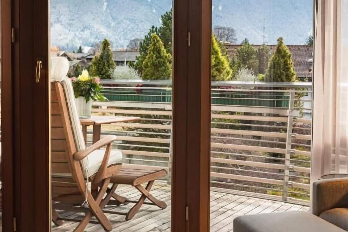 Ein Zimmer mit einer Holzterrasse, einem Stuhl und Blick auf schneebedeckte Berge.