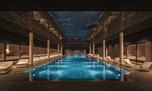 A modern indoor pool with a clear ceiling, lounge chairs, and a central seating area. - Althoff Seehotel Überfahrt (Rottach-Egern)