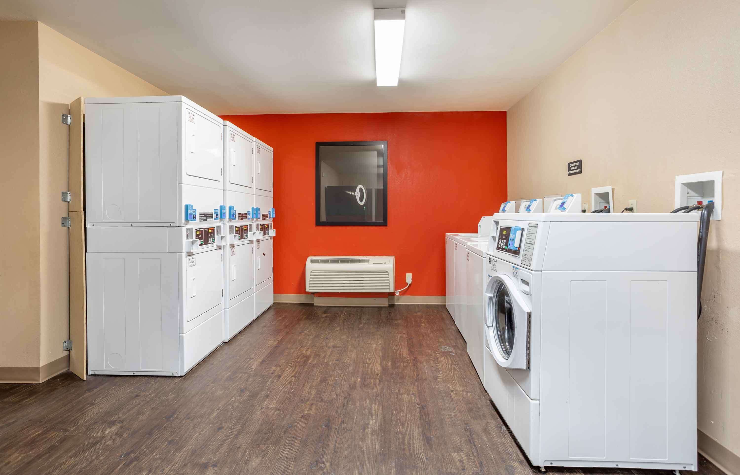 Une buanderie avec des lave-linge et des sèche-linge blancs, un mur rouge et une bouche d’aération.