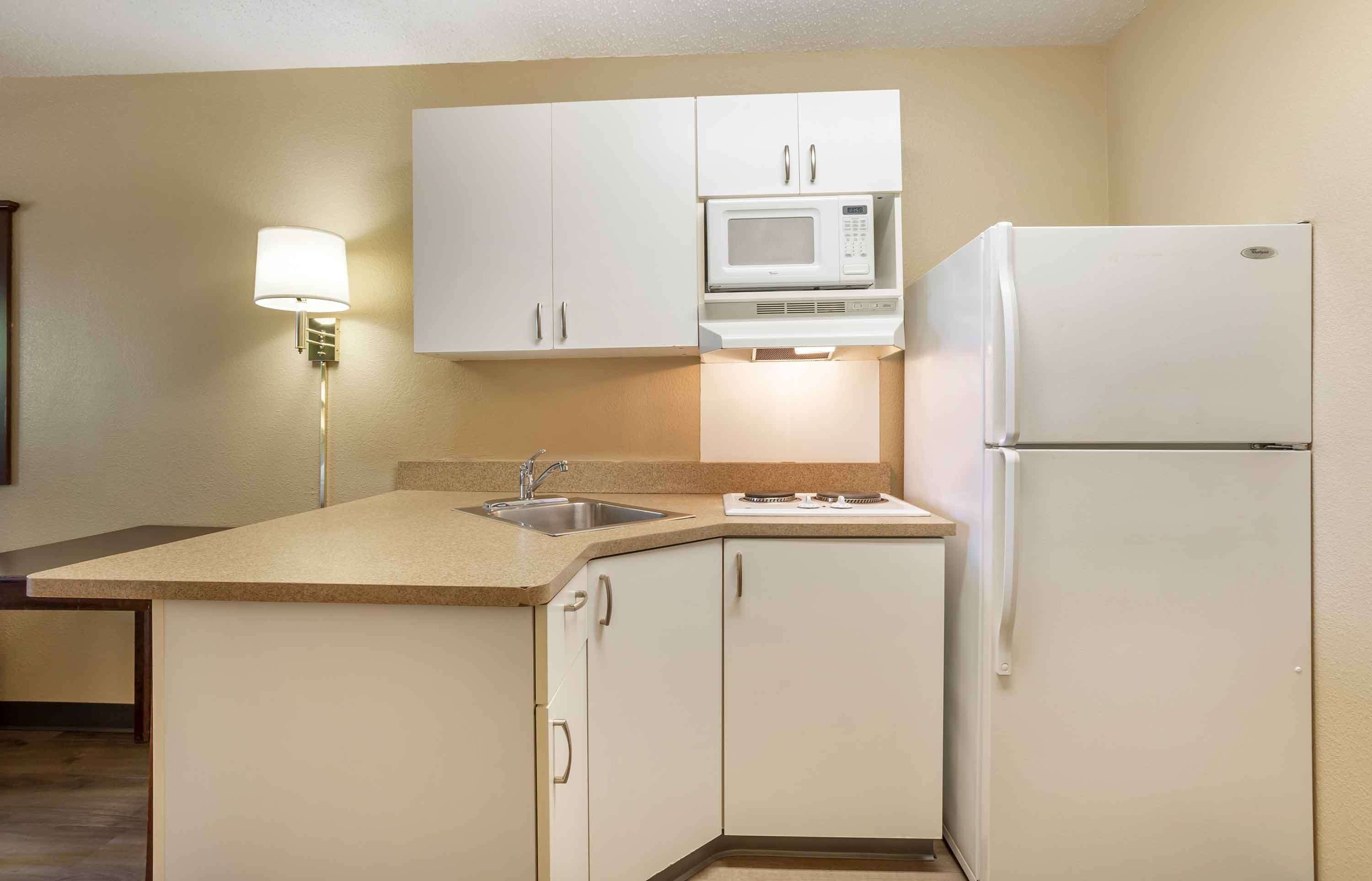 A compact kitchen with white cabinets, a microwave, a refrigerator, a sink, and a stove.