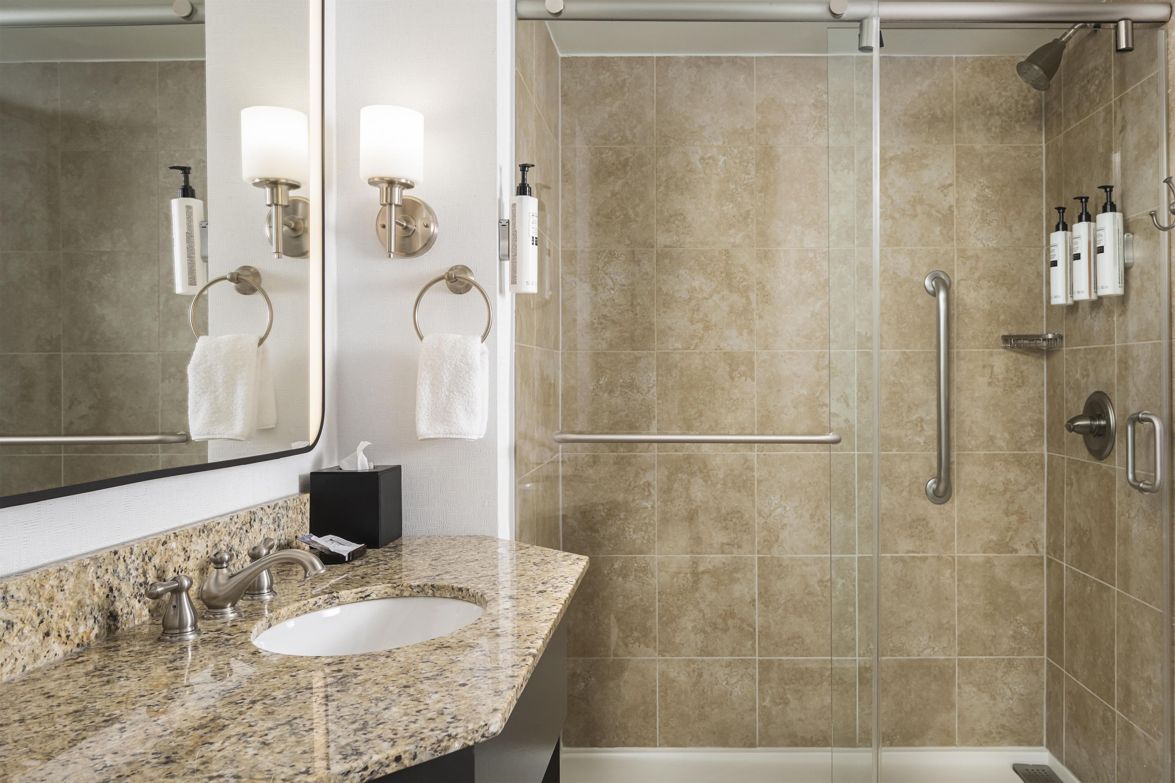 A bathroom with a sink, mirror, towel rack, and shower area.