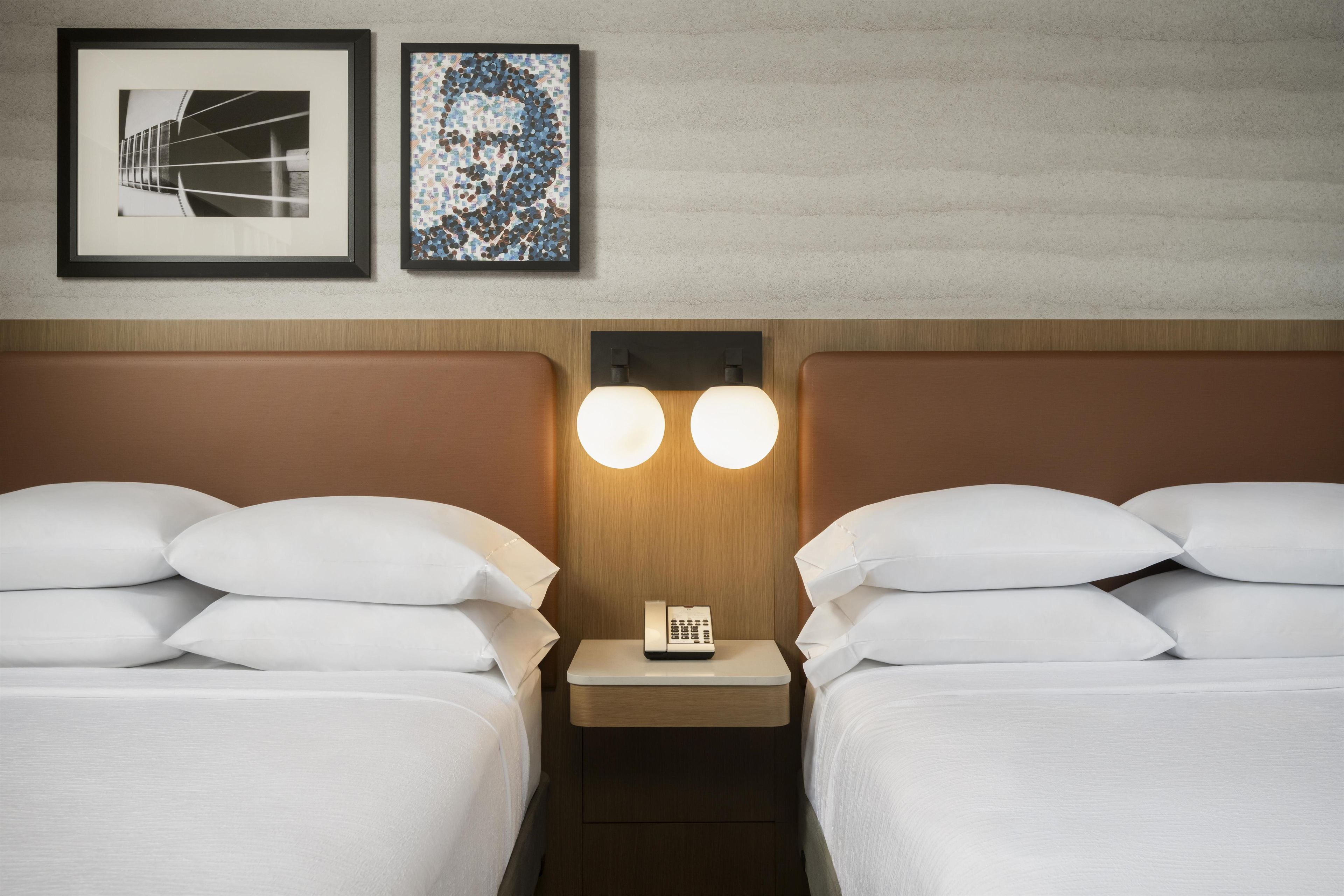 A hotel room with two beds, a nightstand with a phone, and two wall-mounted lamps.