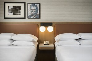 Une chambre d’hôtel avec deux lits, une table de chevet avec un téléphone et deux lampes fixées au mur.