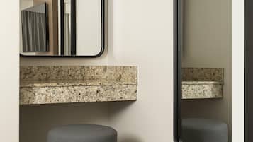 A bathroom with a granite countertop, a mirror, and a grey ottoman.