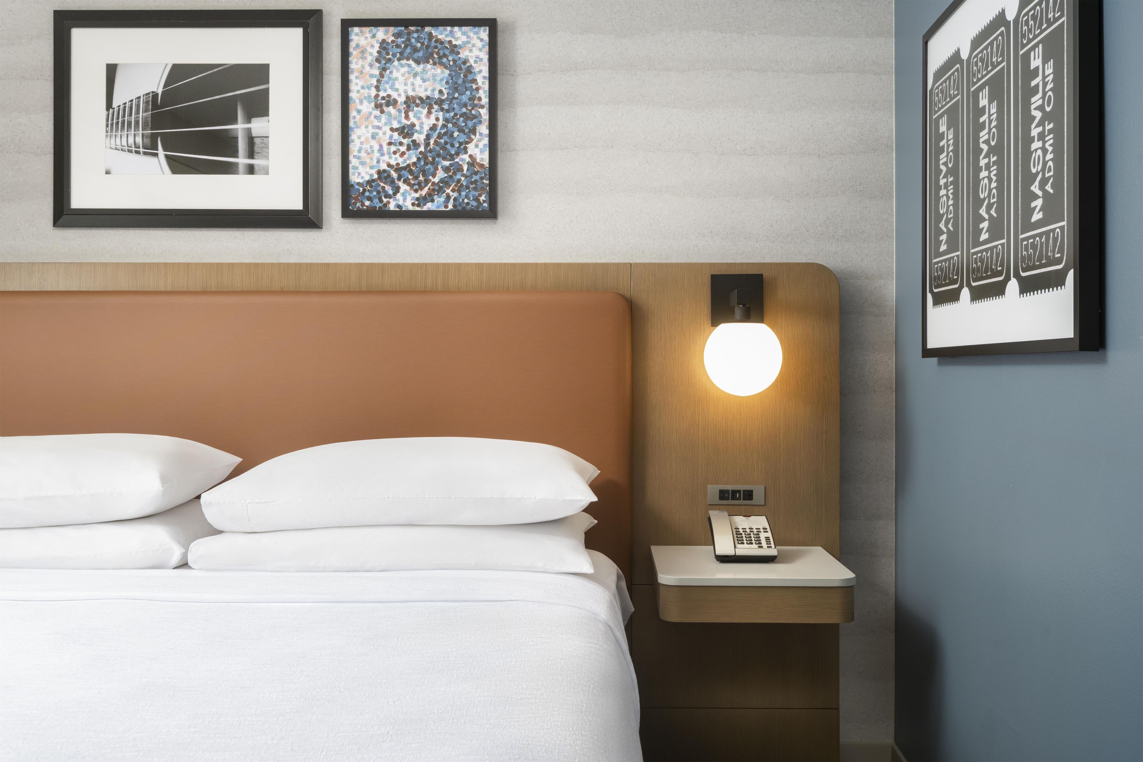 A hotel room with a bed, a bedside table with a phone, and wall-mounted artwork.