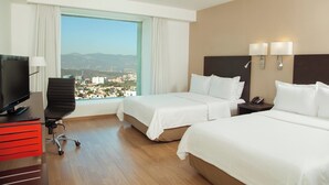 A hotel room with two beds, a desk with a TV, a chair, and a view of a cityscape. - Fiesta Inn Periferico Sur (Mexico City)