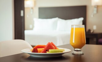 Une chambre d’hôtel avec un lit soigneusement fait, une table de chevet sur laquelle se trouve une assiette de fruits et un verre de jus d’orange.