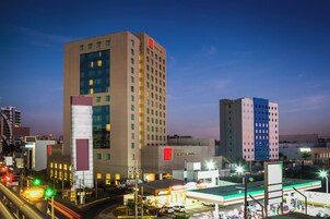 Un hôtel à plusieurs étages, reconnaissable à son grand panneau « Fiesta Inn », doté d’un parking et d’une station-service avec des pompes à essence bien visibles.