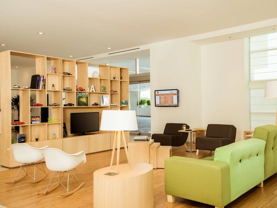 A modern living room with a television, wooden shelving with toys, and green and black furniture.