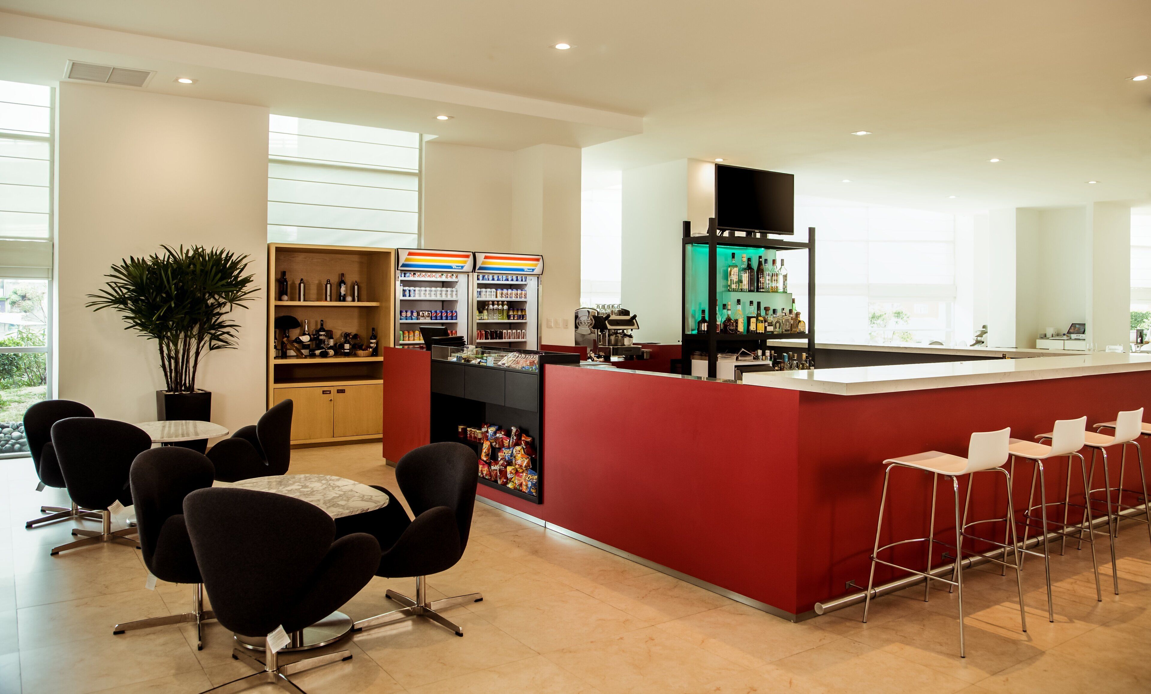 Zona de bar moderna con mostrador rojo, asientos y estanterías llenas de bebidas.