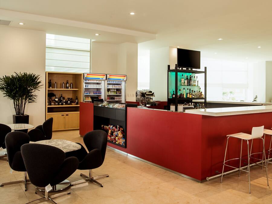 Zona de bar moderna con mostrador rojo, asientos y estanterías llenas de bebidas.
